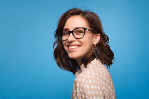 A woman with brown hair wearing glasses and a polka-dot shirt smiling at the camera
