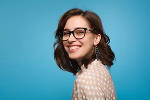 A woman with brown hair wearing glasses and a polka-dot shirt smiling at the camera