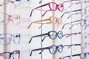 Several pairs of eyeglasses in different colors and styles are displayed on a white wall.