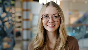 A young blonde woman with glasses smiling for a photo in a modern building.