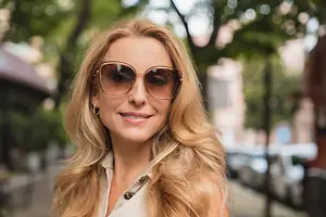 Portrait of a woman with blonde hair wearing sunglasses and a white top on a sunny day