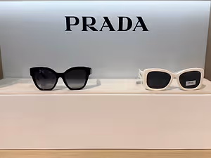A pair of Prada sunglasses in black and white with a Prada logo in the background