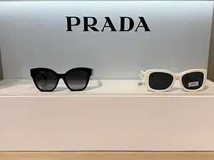 A pair of Prada sunglasses in black and white with a Prada logo in the background