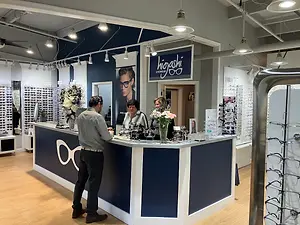 A man and two women stand in front of a counter in an eyeglasses shop.