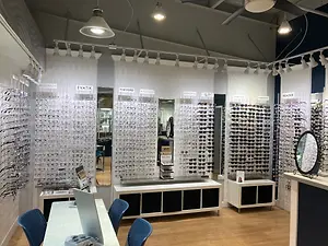 An optical shop with a variety of frames on display and a woman standing in the background.