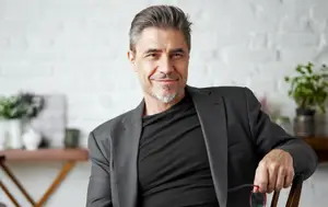 Smiling man with gray hair and beard sitting in a chair looking at the camera