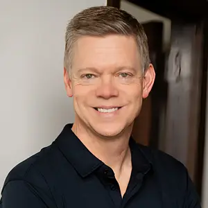 A man with short hair wearing a black polo shirt and smiling for a photo