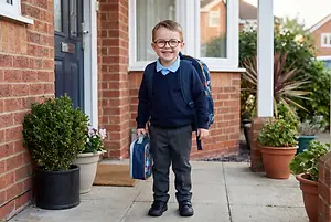 boy wearing glasses and a backpack standing in front of a house