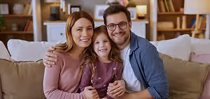 A family of three people sitting on a couch, smiling, and looking at the camera.