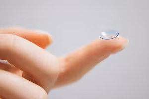 A finger holding a transparent contact lens with a blue outline