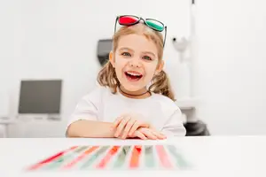 A young girl wearing glasses is sitting at a table in a medical clinic, smiling and posing for a photo.