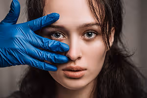 woman getting her nose pierced with blue gloves on