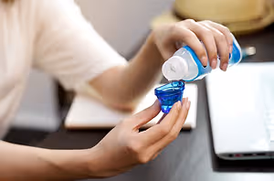 A woman is pouring mouthwash from a bottle into a blue cup.