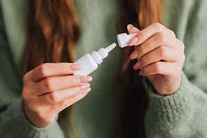 A woman holding a white bottle of eye drops in her hands