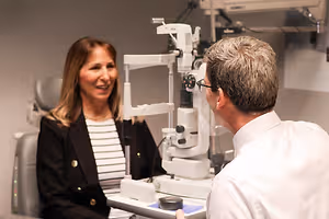 A woman sitting in an optometrist chair while the doctor looks into an ophthalmoscope
