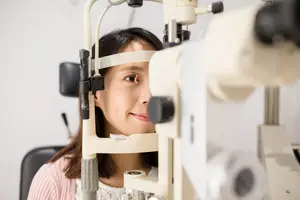 A young woman in a white sweater has her eyes examined by an optician using an ophthalmic instrument