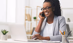 A woman sitting at a desk talking on a cellphone while smiling