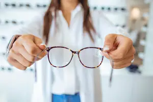 A woman is holding a pair of eyeglasses with brown frames.
