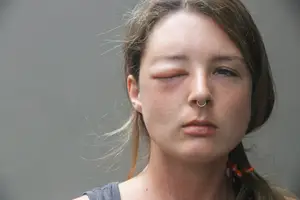 A close up of a woman with one eye closed and wearing a nose ring.