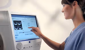 A nurse points at an eye chart displayed on a medical monitor in a clinical setting.