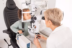 A young girl is having her eyes examined by an optometrist in an exam room.