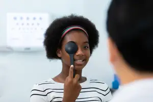 A young girl with a black eye patch is looking at a doctor with a smile on her face.