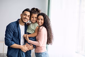 A family of three is smiling and posing for a photo in a room.