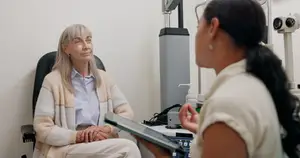 A woman consults with an eye care professional, discussing her vision and possible treatments, seated in a clinical setting.