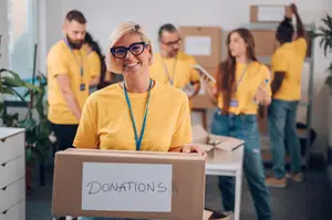 Volunteers in yellow shirts are collecting donations in a room with a desk and storage boxes