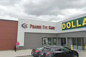 A storefront with a Prairie Eye Care sign and a Dollar sign on the right side with a person standing outside on a cloudy day.