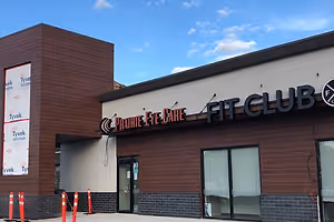 A storefront for Prairie Eye Care and Fit Club with wooden panels and a sign, under a cloudy sky.