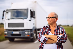 A smiling man in glasses is standing in front of a white truck in a field