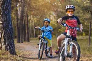 Two kids riding bicycles on a forest trail with trees in the background