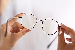 A person is holding a pair of eyeglasses with a brown frame and clear lenses.