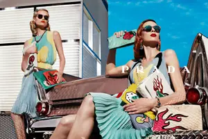 Two women wearing sunglasses and holding Prada bags, sitting on a vintage car with the word Prada on the side