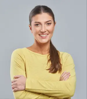 A woman with a smile on her face and arms crossed in front of her chest wearing a yellow long-sleeve shirt