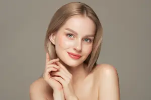 A woman with blonde hair and blue eyes is posing for a picture with her hands on her cheeks.