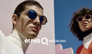 Two people wearing sunglasses standing next to each other with a pink wall and blue sky in the background