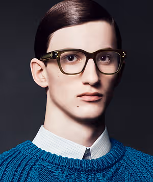 A man with short brown hair wearing glasses and a blue sweater with a white collared shirt underneath.