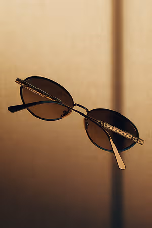 A pair of sunglasses with brown lenses and a golden frame rest on a beige surface, capturing a shadow of light and casting a shadow on the background.