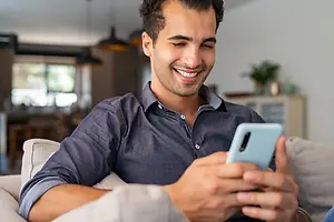 Smiling man using a smartphone while relaxing on a sofa