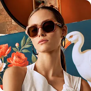 Woman wearing oversized brown sunglasses in front of a colorful floral and swan mural