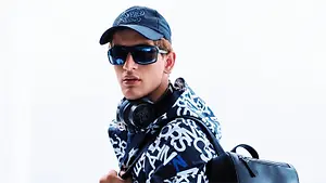 Young man wearing dark sunglasses, a blue cap, patterned jacket, and headphones