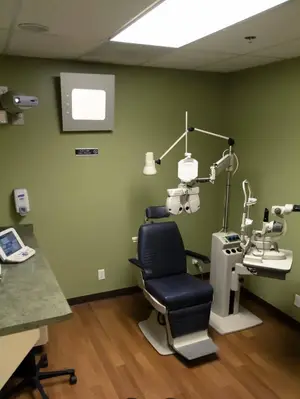 Interior of an eye care examination room with a reclining chair, medical equipment, and a projector.
