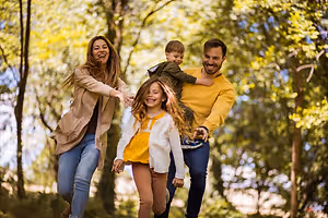 A family is walking and playing in the forest with a young boy riding on his father's back