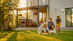 A family playing with a dog in the yard of a house in the evening