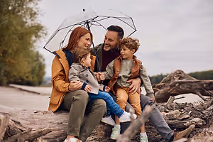 Family of four sitting on a log in the rain with an umbrella