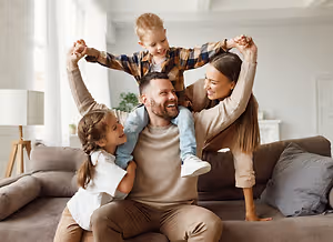 A family is sitting on a couch with a lamp and a plant in the background.