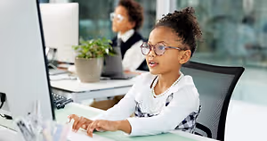 Girl sitting at a desk with a computer in front of her in an office.