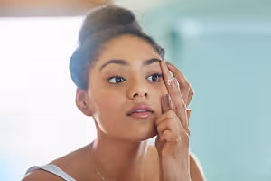 A woman applying a transparent product on her face in a bathroom